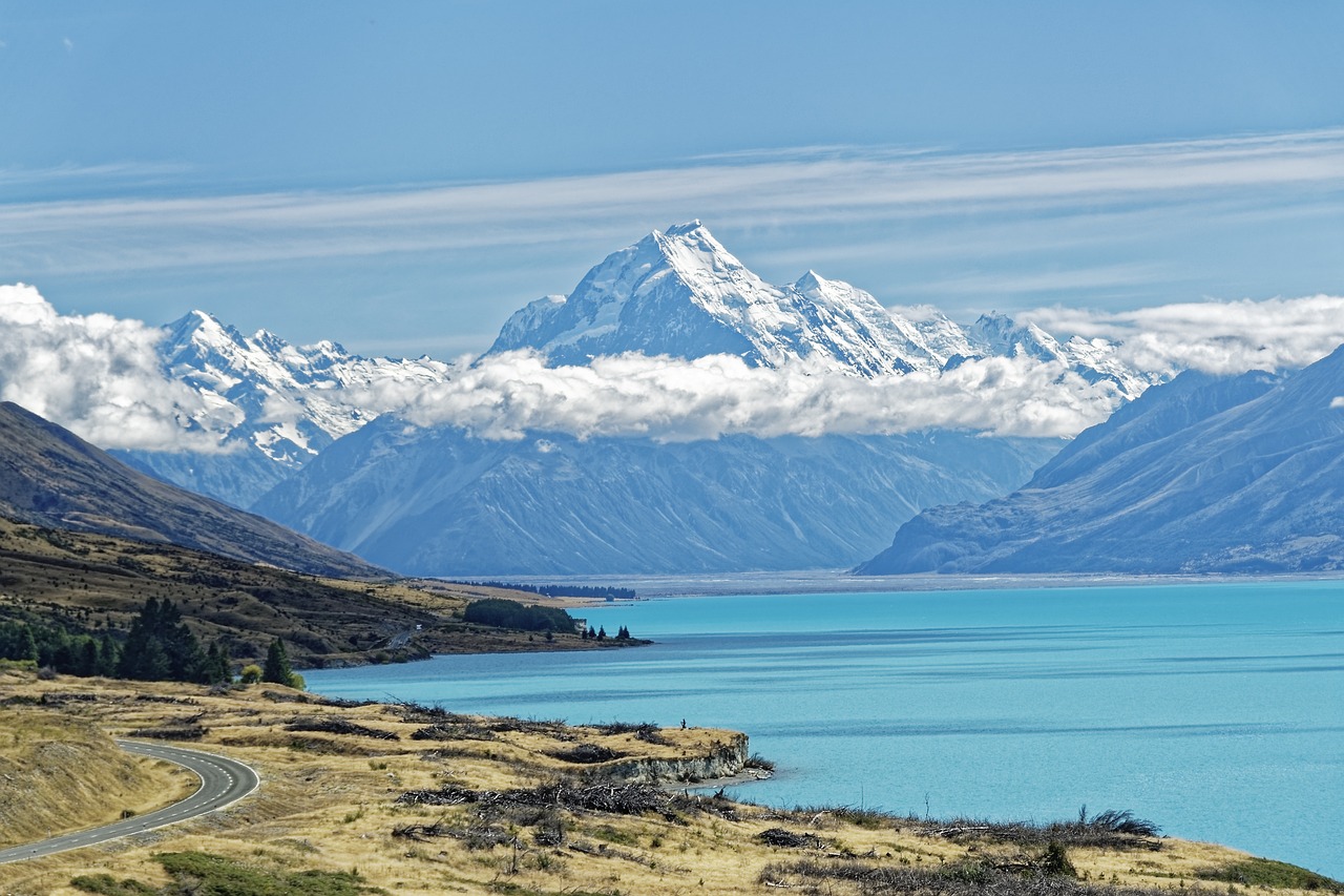 Blick auf einen See mit einer Straße im Vordergrund und einer Gebirgskette im Hintergrund